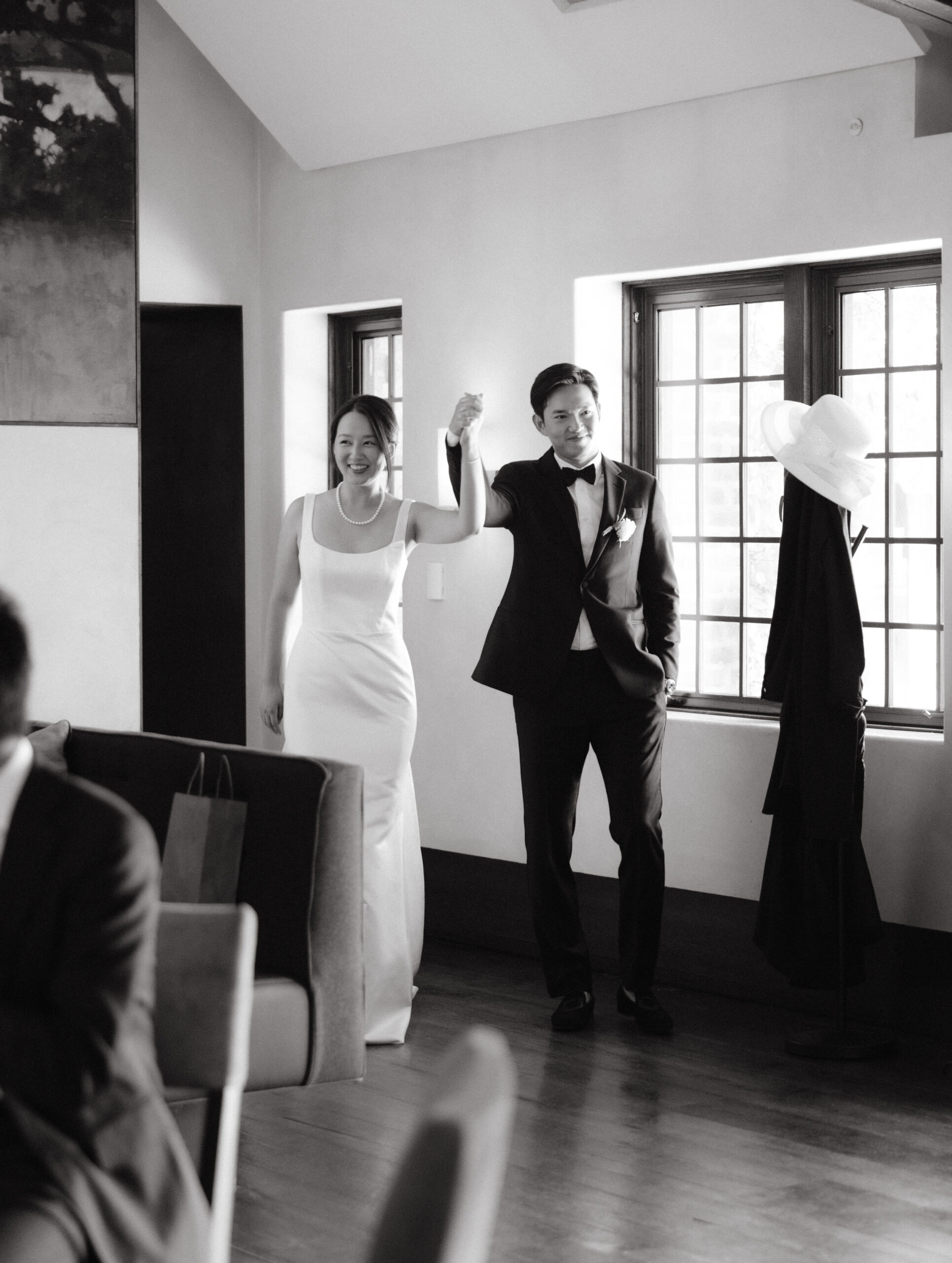 Black and white image of the newlyweds happily entering the reception area, captured by Jenny Fu Studio