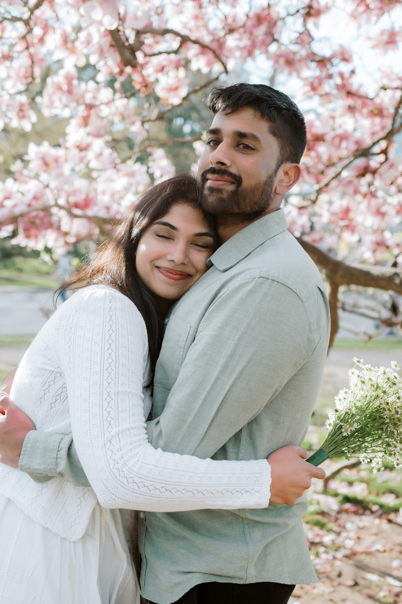The engaged couple are happily hugging each other with a cherry blossom in the background. Image by Jenny Fu Studio