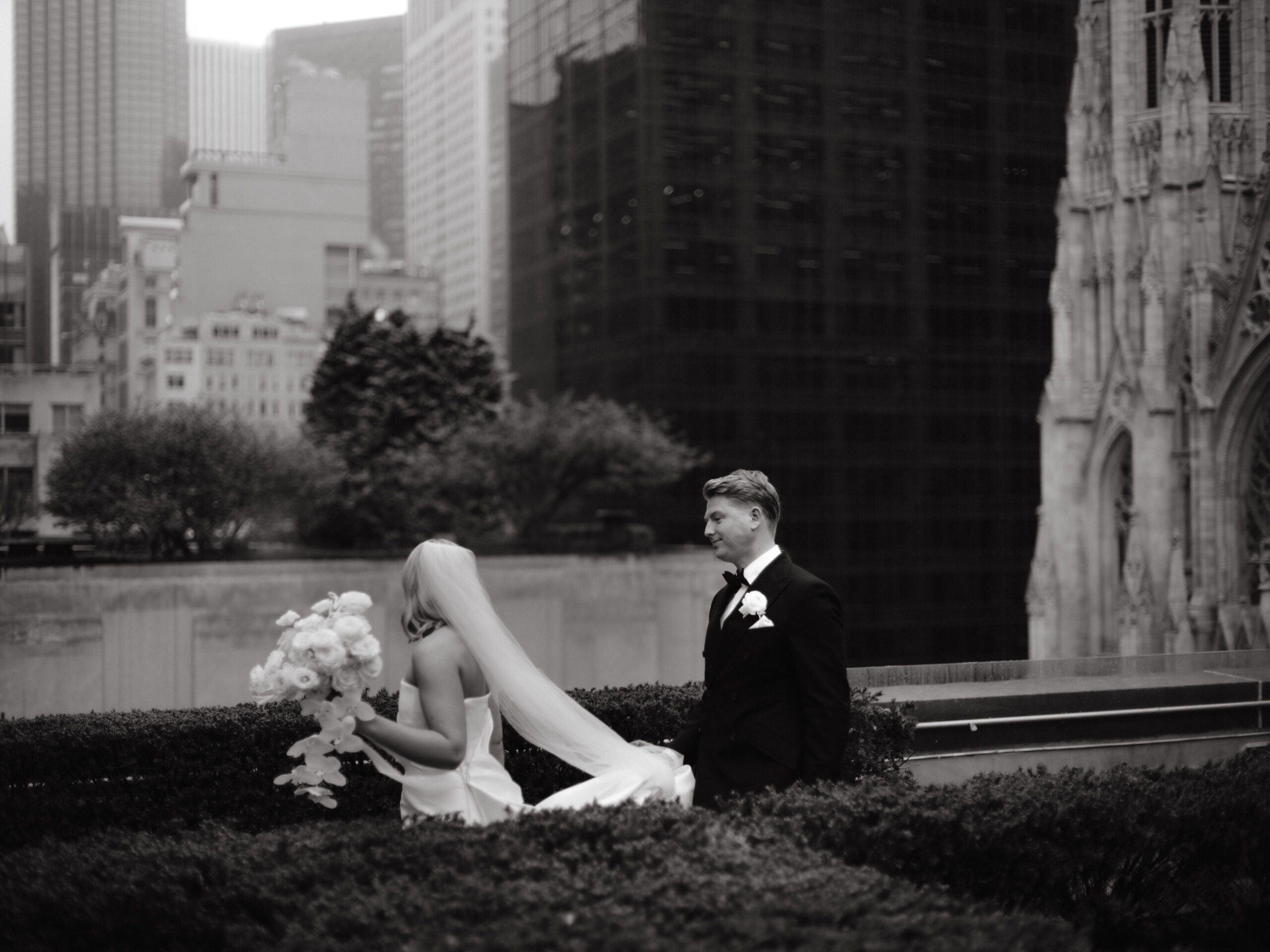 Black and white candid image of the newlyweds in 620 Loft and Garden, NYC, with stunning skyscrapers in the background. Image by Jenny Fu Studio