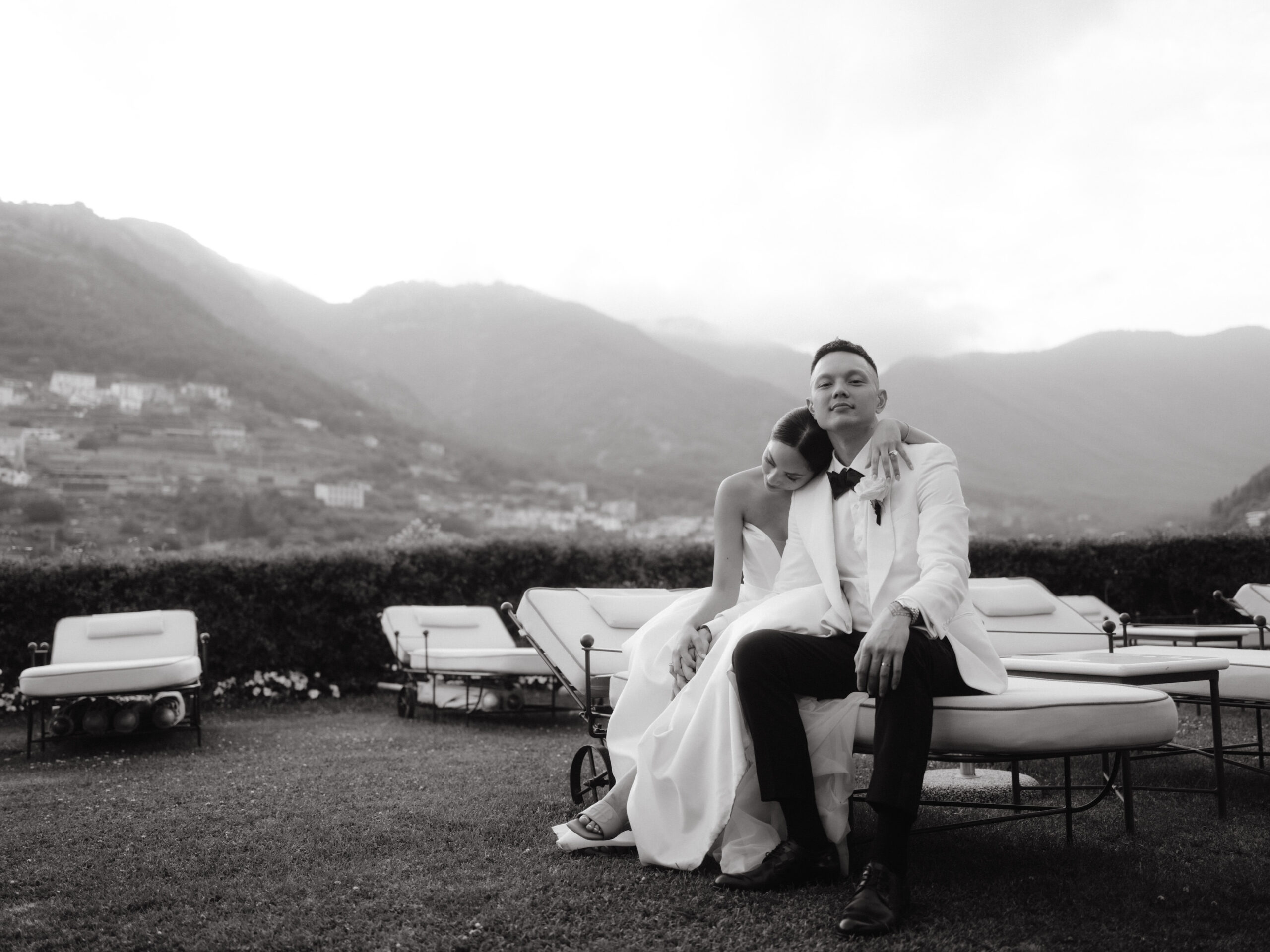 Black and white image of the bride and groom relaxing outside of the villa with mountains in the background. Wedding in Italy image by Jenny Fu Studio