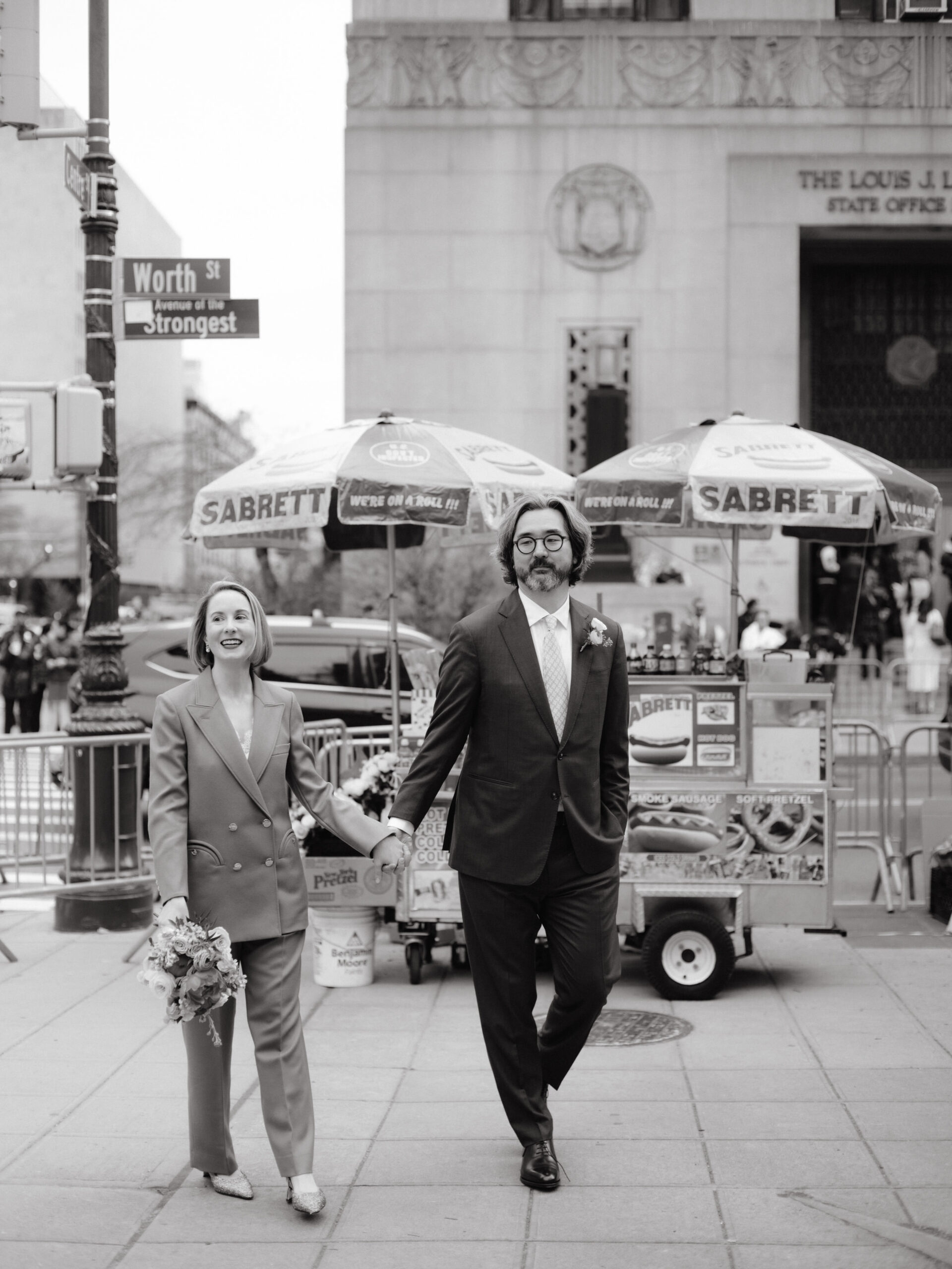 The bride and groom are walking along Worth St. in New York on their way to the City Clerk's office for their wedding. NYC City Hall Elopement image by Jenny Fu Studio