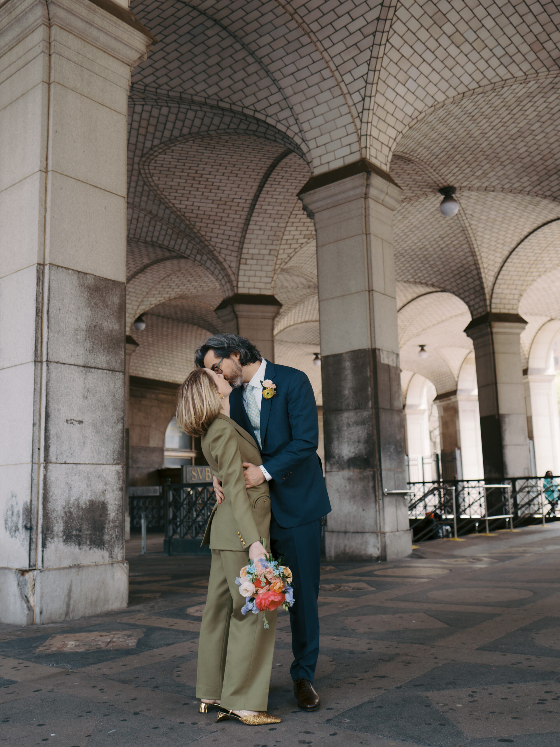 The newlyweds are kissing in the subway station with timeless architecture in the background. Image by Jenny Fu Studio