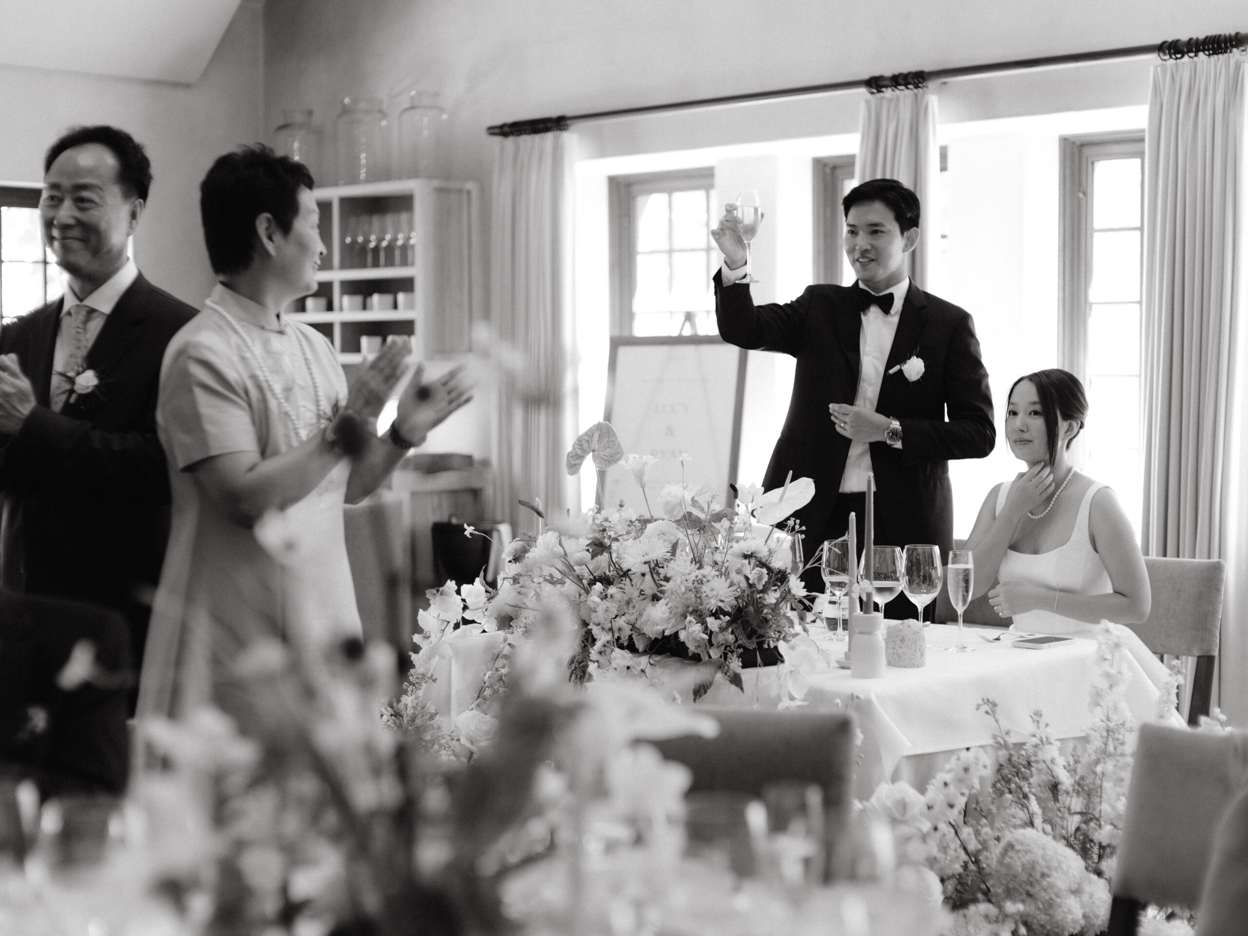 A black and white candid image of the newlyweds giving a toast at their wedding reception, captured by Jenny Fu Studio.