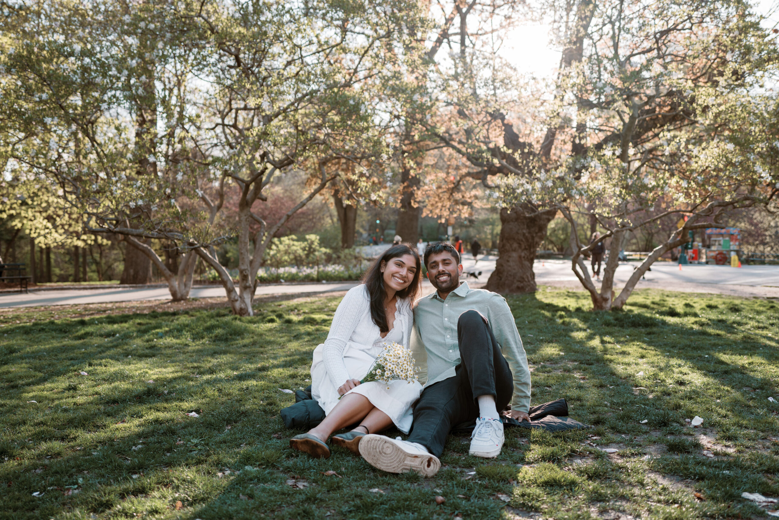 The engaged couple is happily sitting on the grass in Central Park, NYC, in spring. Image by Jenny Fu Studio