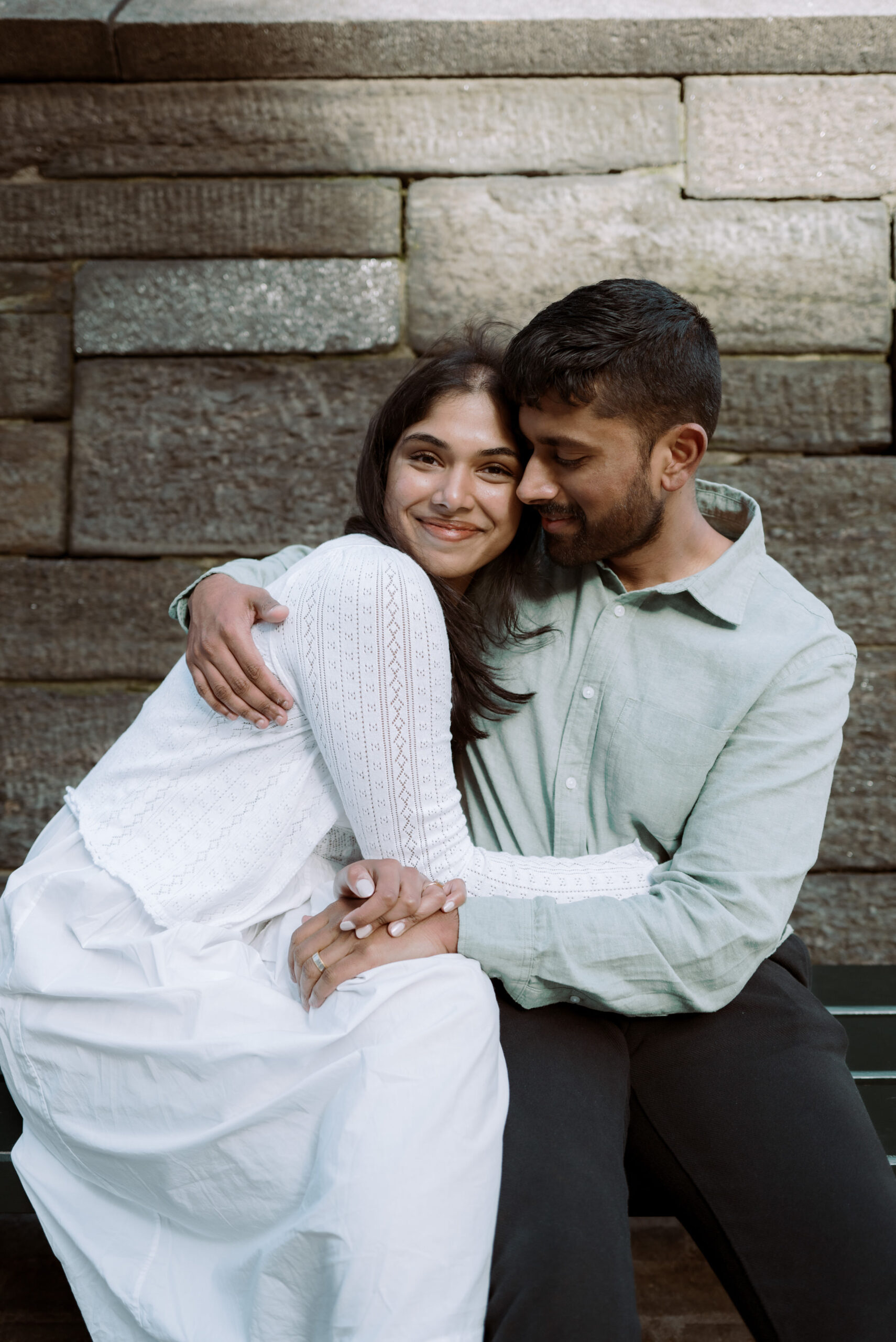 The engaged couple is lovingly hugging each other with a stone wall in the background. Image by Jenny Fu Studio 