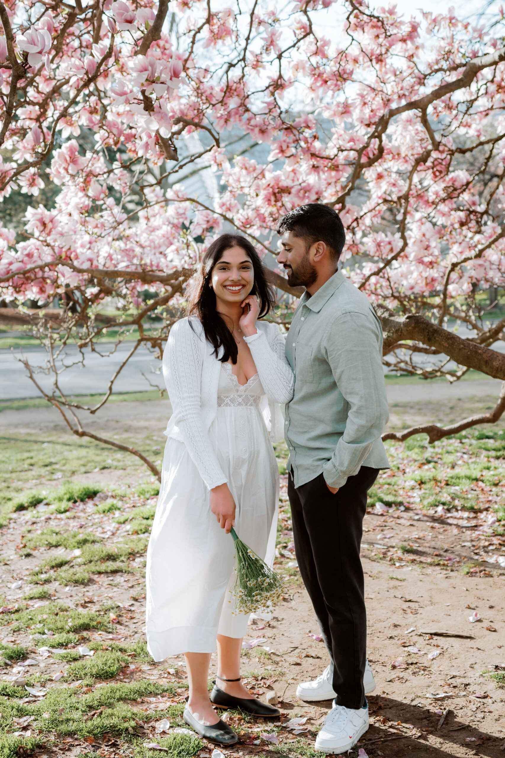 The fiancé lovingly looks at his fiancée as she smiles at the camera amidst cherry blossoms in spring, captured by Jenny Fu Studio