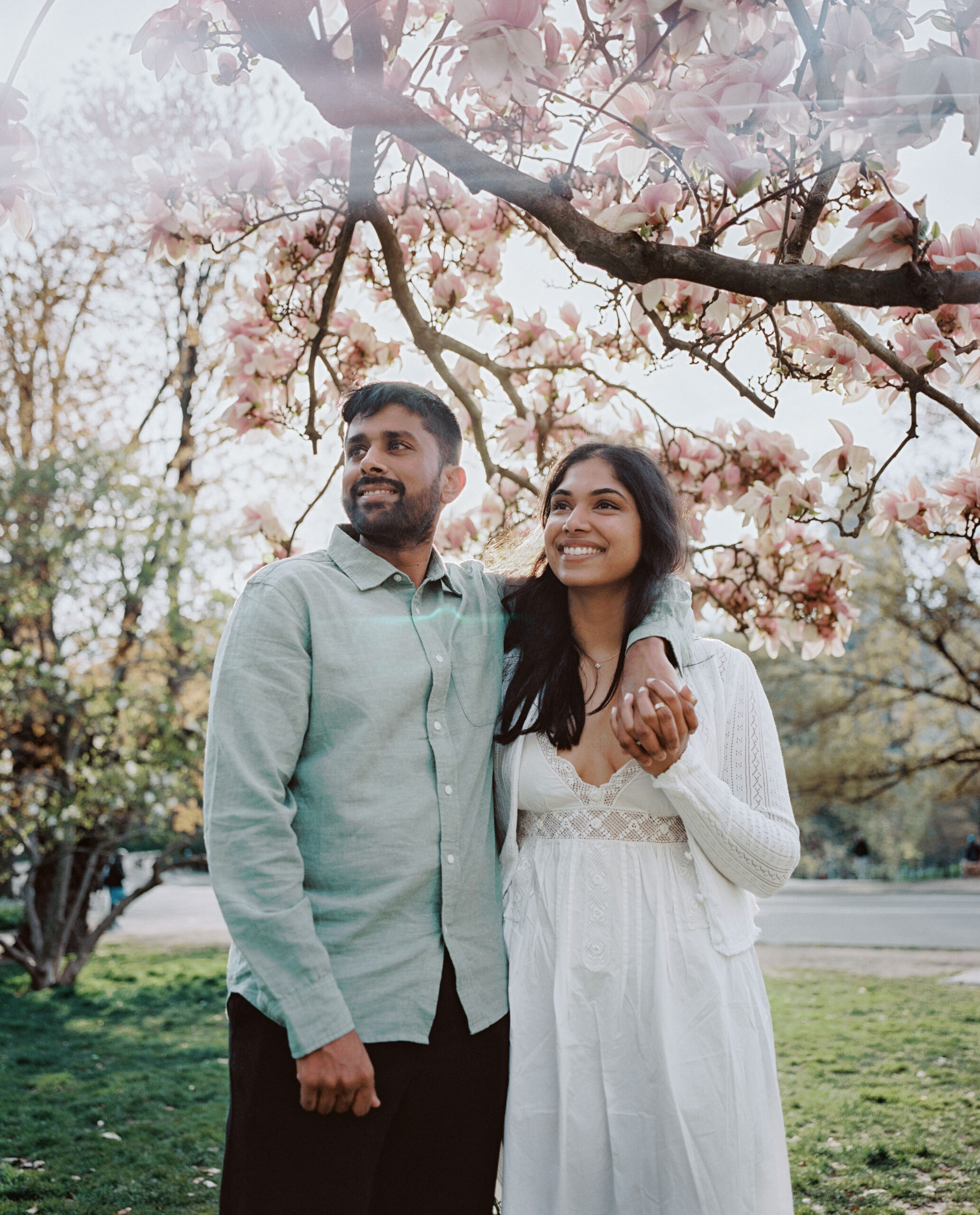 A happily engaged couple with a beautiful cherry blossom tree in the background. Engagement photography image Jenny Fu Studio