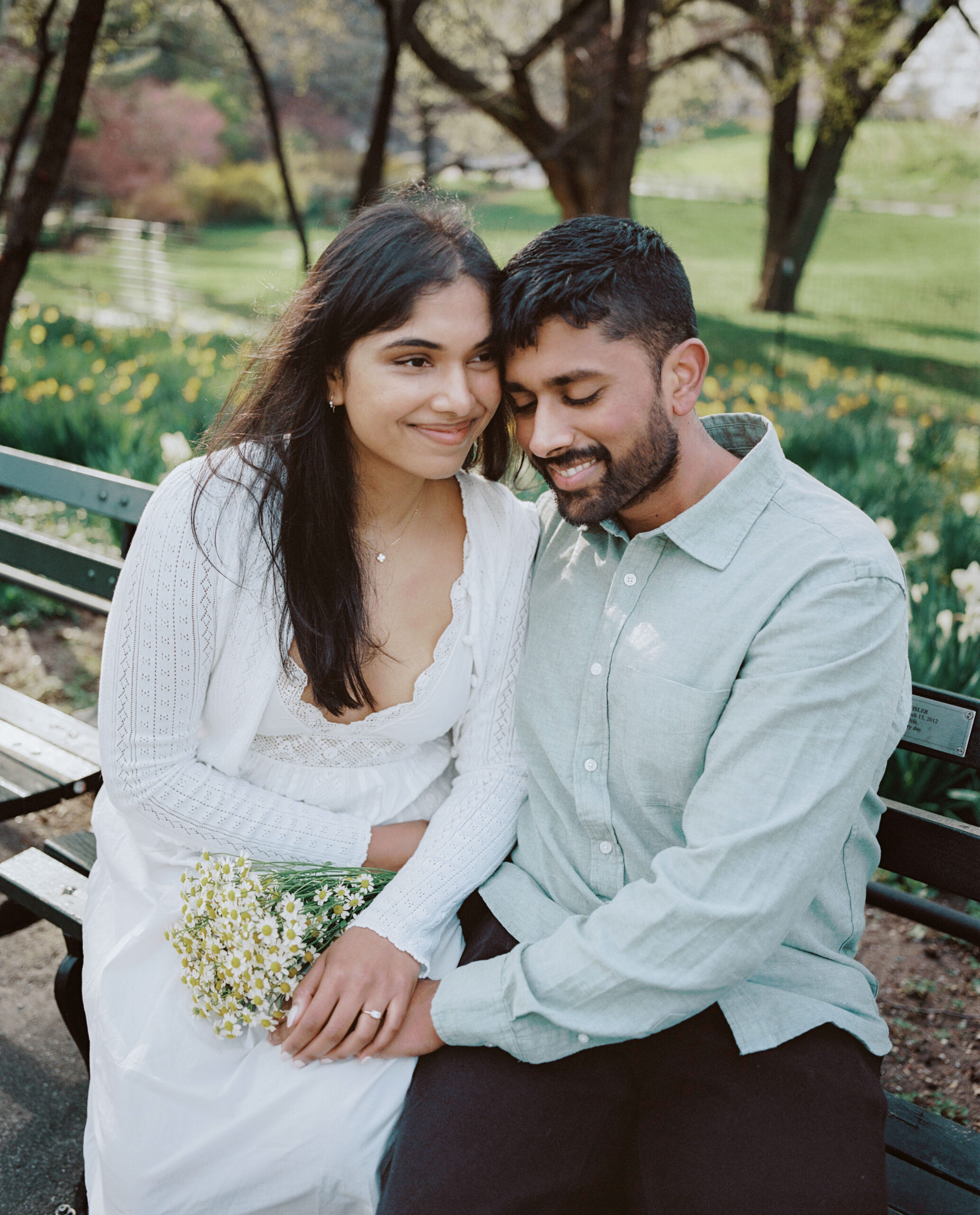 The engaged couple is having a happy, intimate moment while sitting on a bench in Central Park, NYC, beautifully captured by Jenny Fu Studio