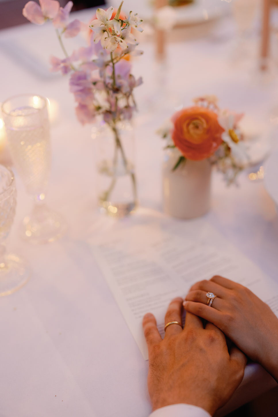 A photo of the  bride and groom's hands holding each other over the wedding reception table, by Jenny Fu Studio.