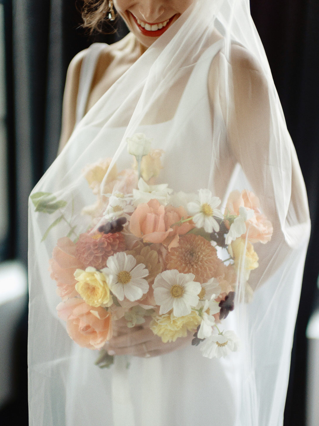 The bride is happily holding her flower bouquet while being enveloped by her veil. Image by Jenny Fu Studio