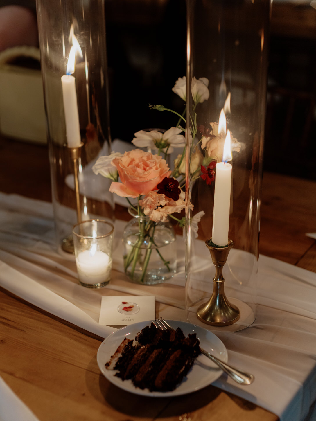 A slice of chocolate wedding cake is on the reception table, with elegant table centerpiece. Luxurious wedding image by Jenny Fu Studio