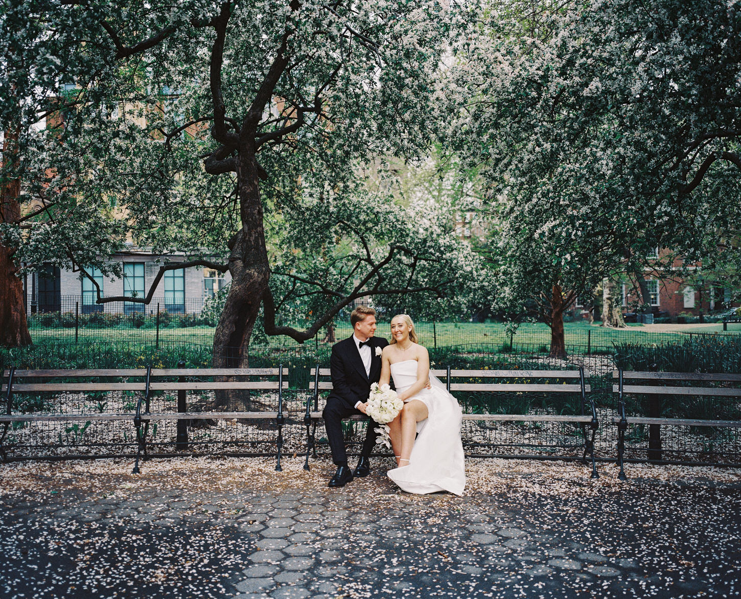 The newlyweds relax at Washington Square Park, sitting on a bench after their elopement in NYC, captured by Jenny Fu Studio.