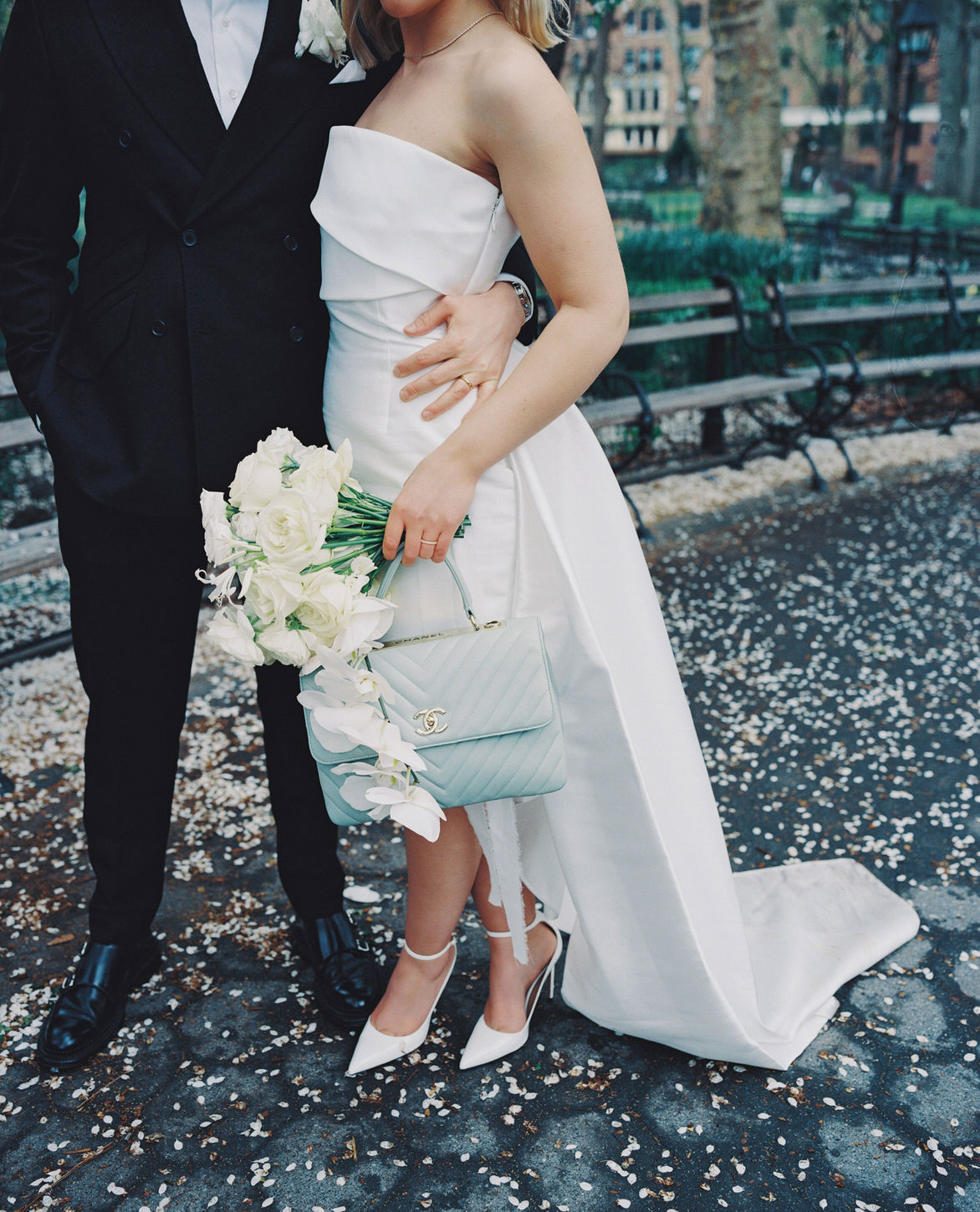 Body shot of the bride holding her Chanel bag and wedding bouquet while standing very close to the groom.