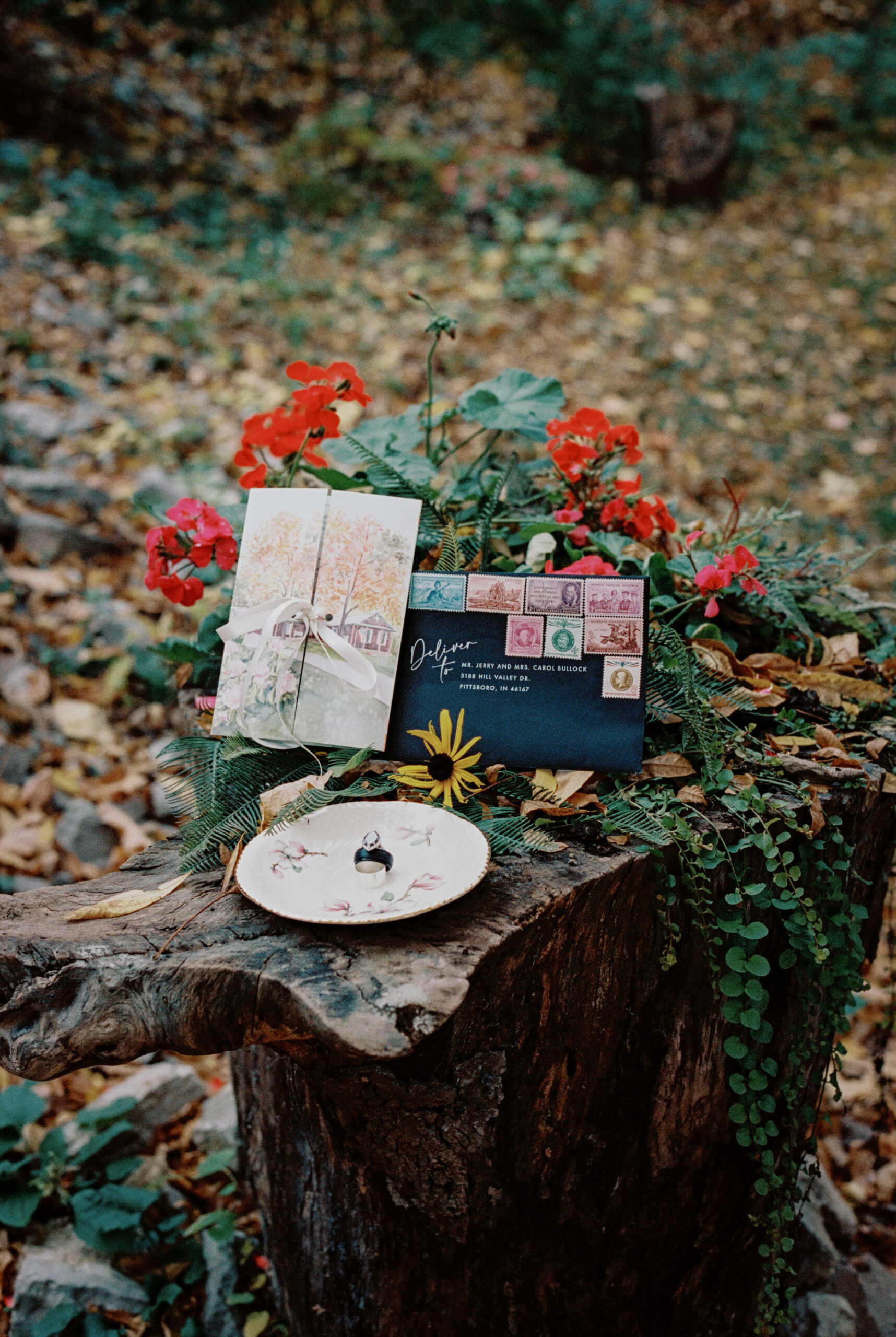 Wedding bands and invitation cards laid out beautifully outdoors with autumn leaves in the background, captured by Jenny Fu Studio.