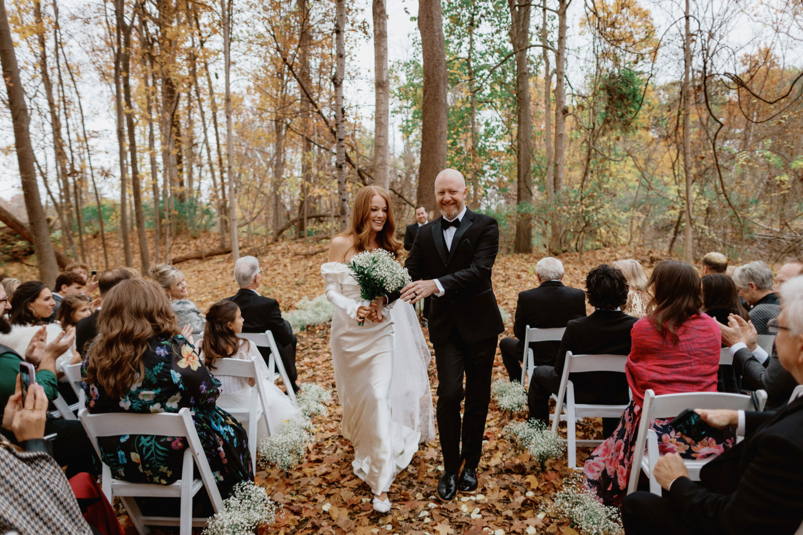 The bride and groom are happily walking back down the aisle after the wedding ceremony outdoors as the guests cheer on, candidly captured by Jenny Fu Studio.