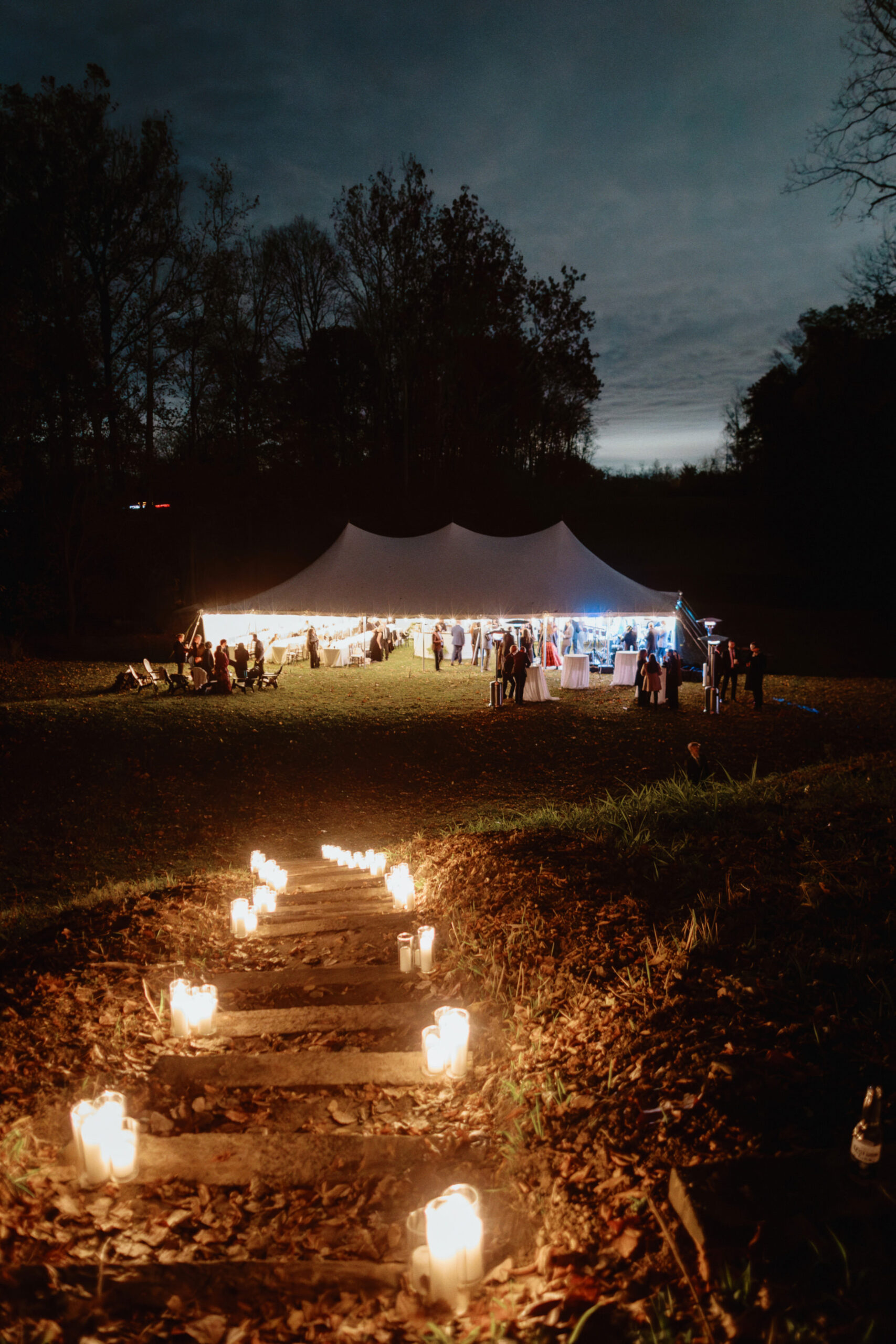 Beautiful night shot of an outdoor wedding reception venue with candles leading to a white tent, shot by Jenny Fu Studio. 