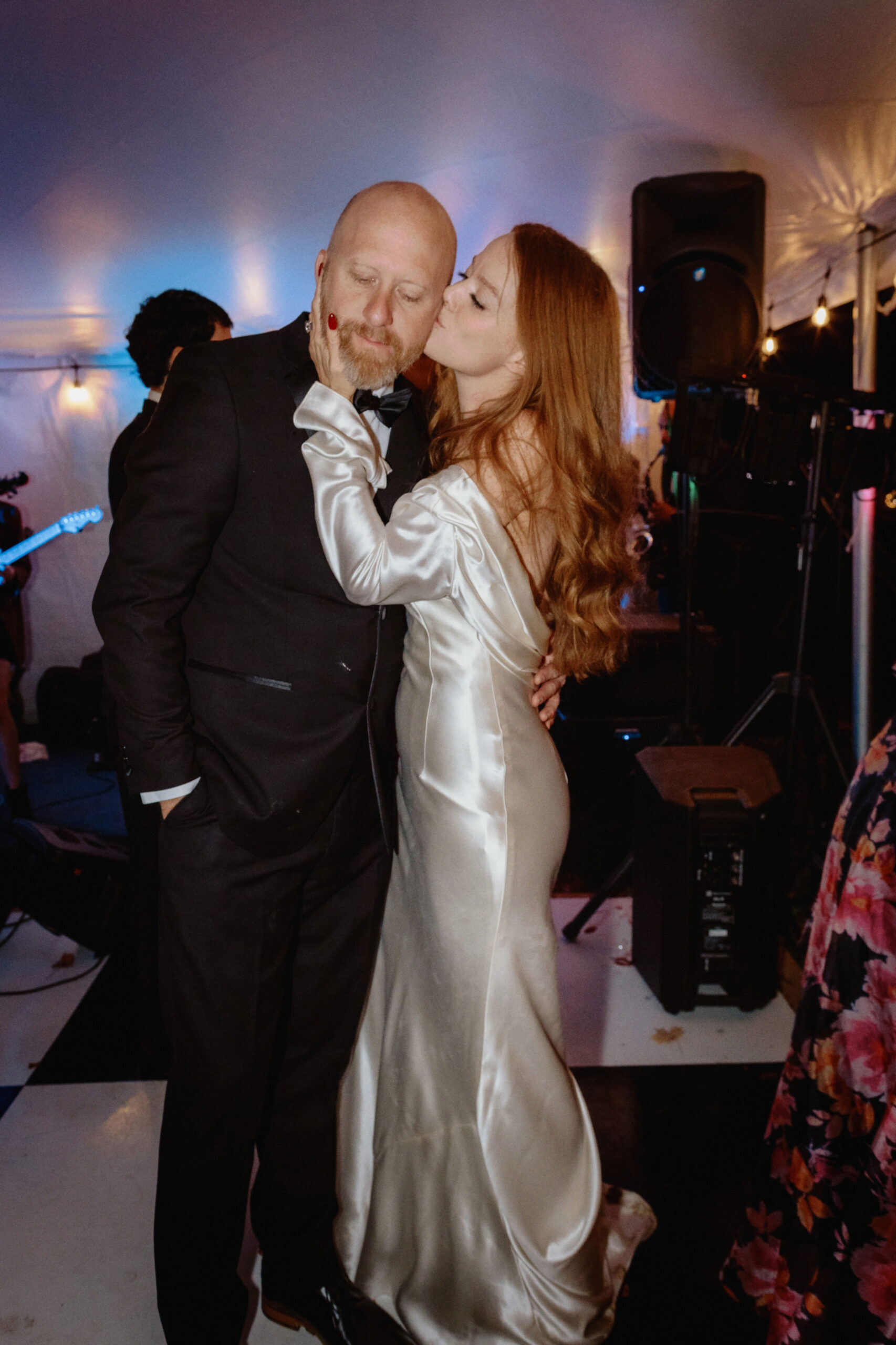 The bride is lovingly giving her groom a  kiss on the cheek in the dance floor, captured by Jenny Fu Studio.