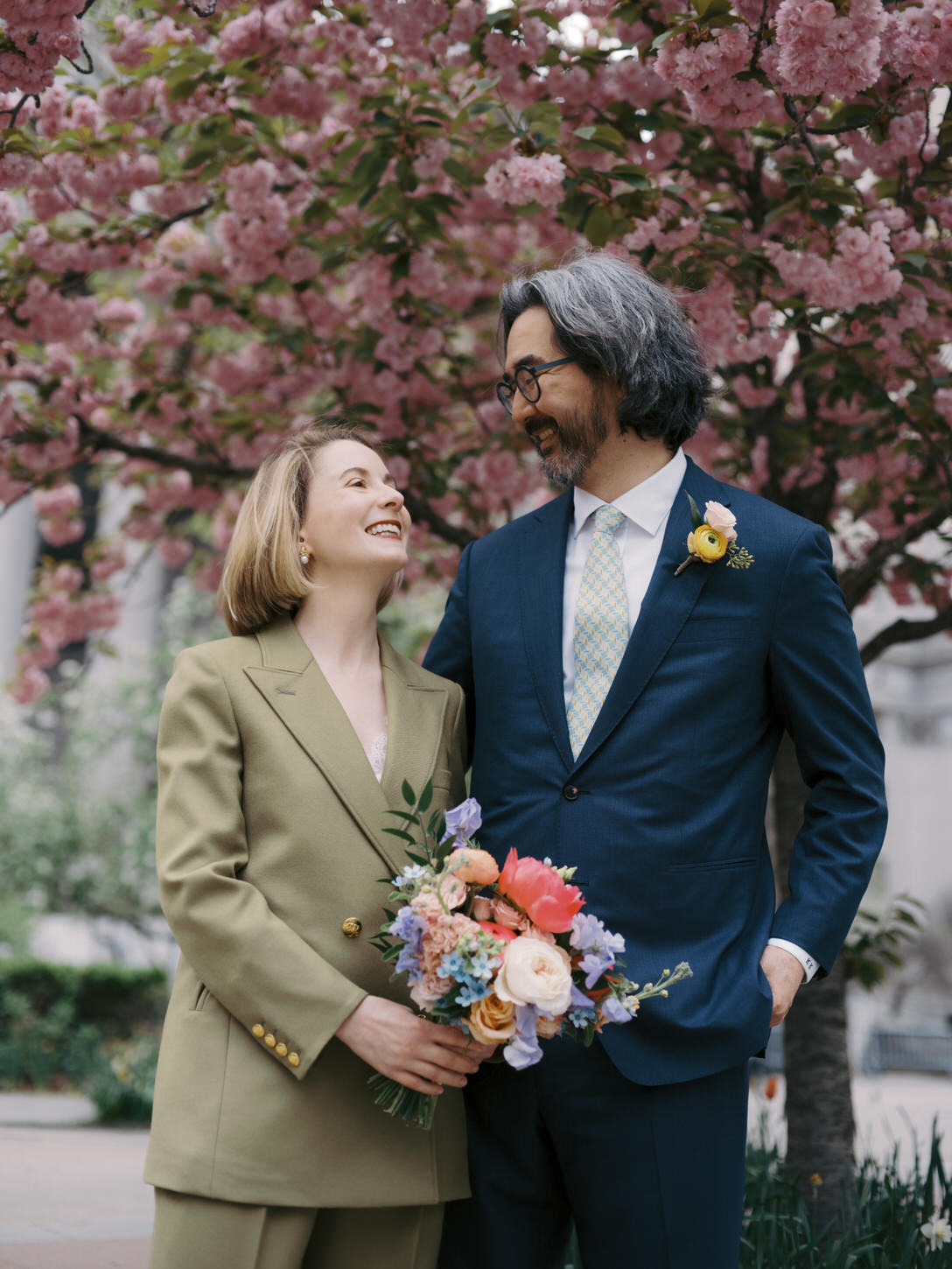 The newlyweds are happily looking at each other with cherry blossom trees in the background shot by Jenny Fu Studio, NYC.