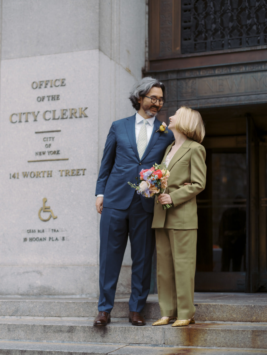 The bride and groom are smiling at each other in front of the City Clerk's Office in Manhattan, shot by Jenny Fu Studio.