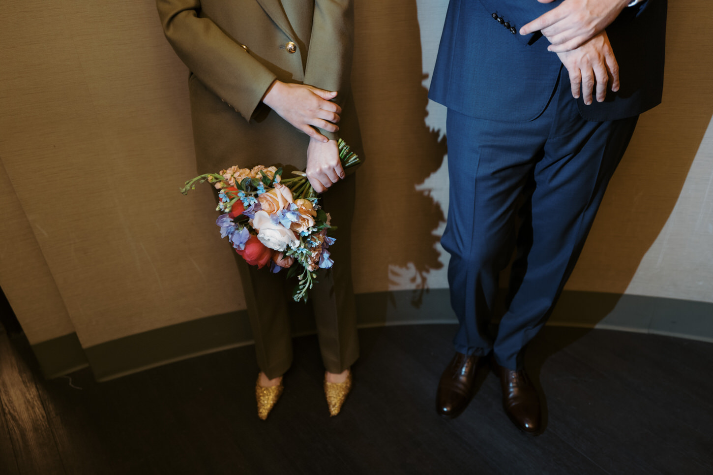 Lower-body shot of the bride and groom, showing their wedding shoes, while waiting for their turn inside NYC City Hall for the wedding ceremony, shot by Jenny Fu Studio.