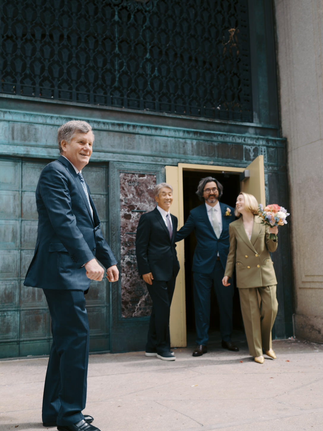 An exit shot of the newlyweds with their fathers after their spring wedding at NYC City Hall, by Jenny Fu Studio.