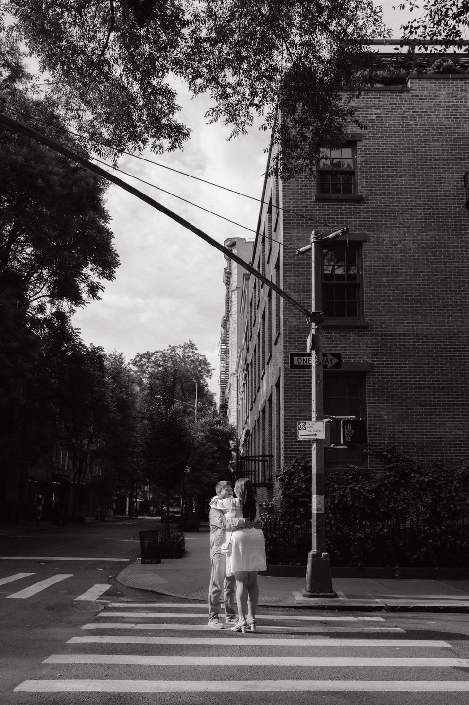 A black and white photojournalistic engagement photo of a couple hugging each other in the streets of West Village, NYC, captured by Jenny Fu Studio.