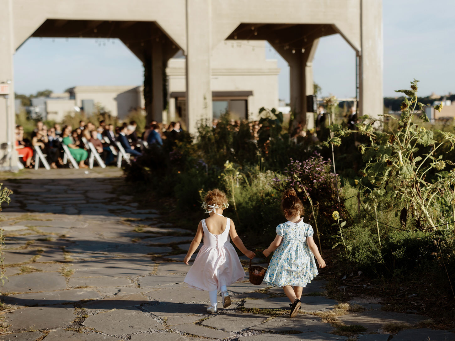 Two cute little flower girls are walking towards the wedding ceremony area in Brooklyn Grange, NY, captured by Jenny Fu Studio. 