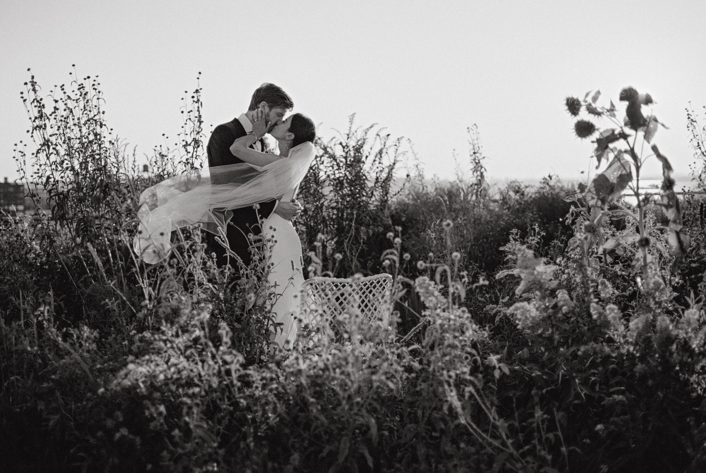 A special black and white portrait of the newlyweds kissing outdoors as the gentle breeze sways the bride's veil, beautifully captured by Jenny Fu Studio.