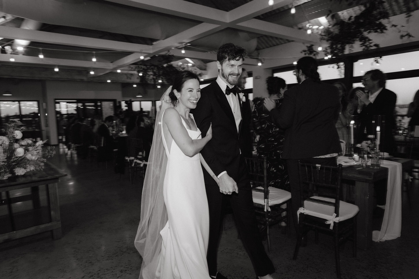 The newlyweds happily enters the wedding reception as the guests welcomes them, in a black and white image captured by Jenny Fu Studio.