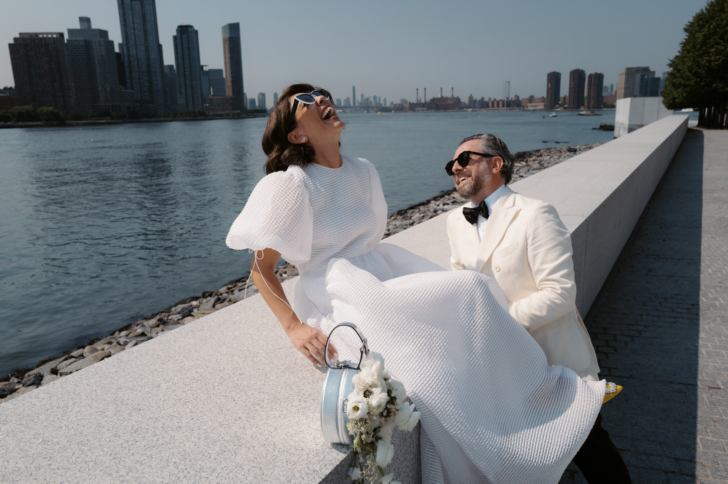 A chic couple is having fun in their elopement  with a river and buildings in the background at Four Freedoms Park, NYC, captured by Jenny Fu Studio.