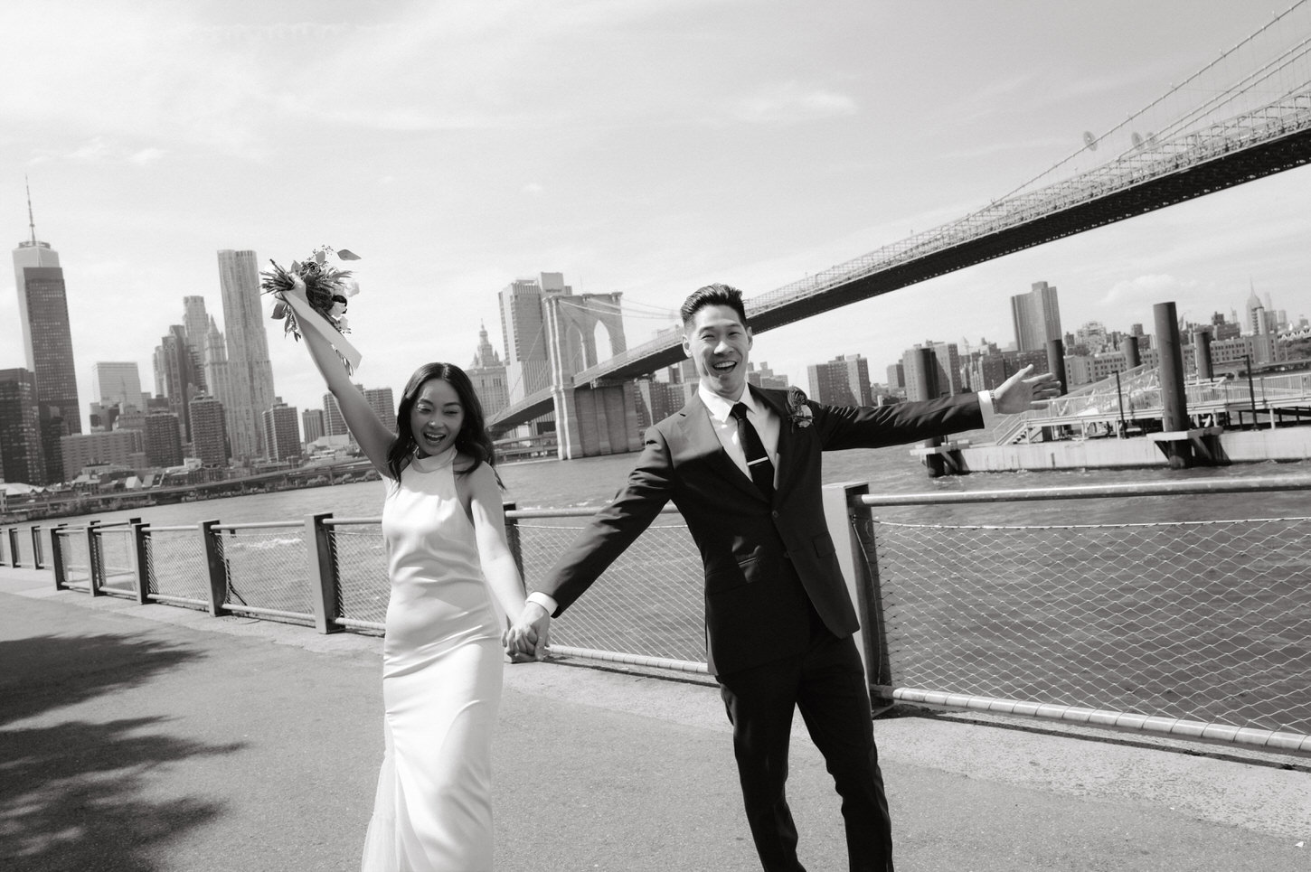 Black and white film photography image of the bride and groom with Brooklyn Bridge in the background captured by Jenny Fu Studio.