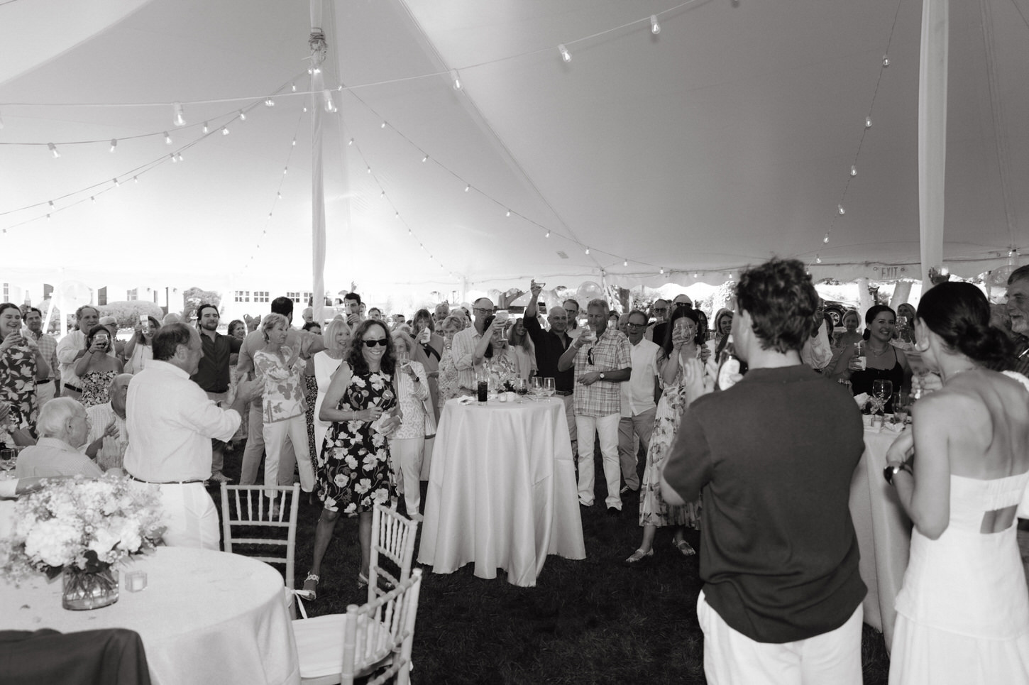 A black and white image of a wedding shower event with the soon-to-be bride and groom and all the guests having a toast, captured by Jenny Fu Studio.