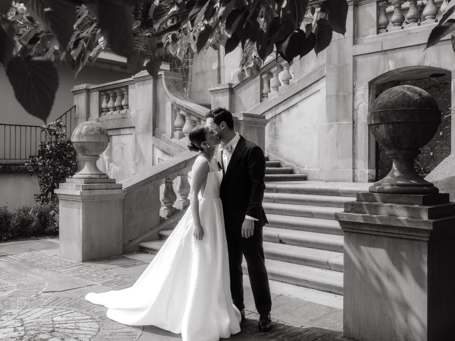 A black and white, candid image of the bride and groom kissing each other on the cheek,  by Jenny Fu Studio.