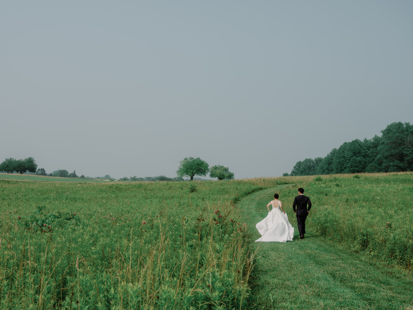 The bride and groom are running on a wide, green field, shot  by Jenny Fu Studio, for a luxury wedding album.