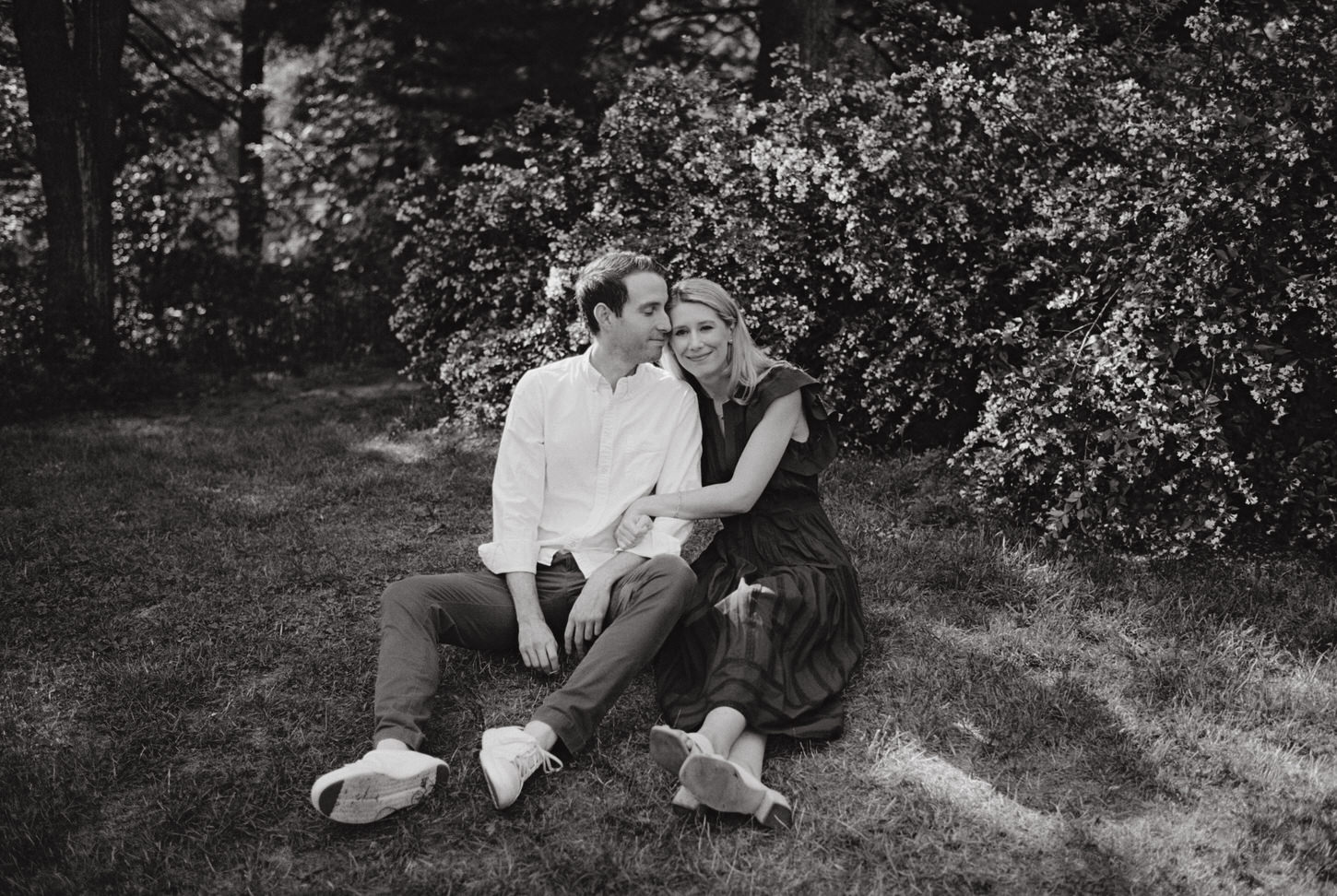 Black and white, timeless image of the engaged couple sitting on the grass at a park in NYC, captured by Jenny Fu Studio. 