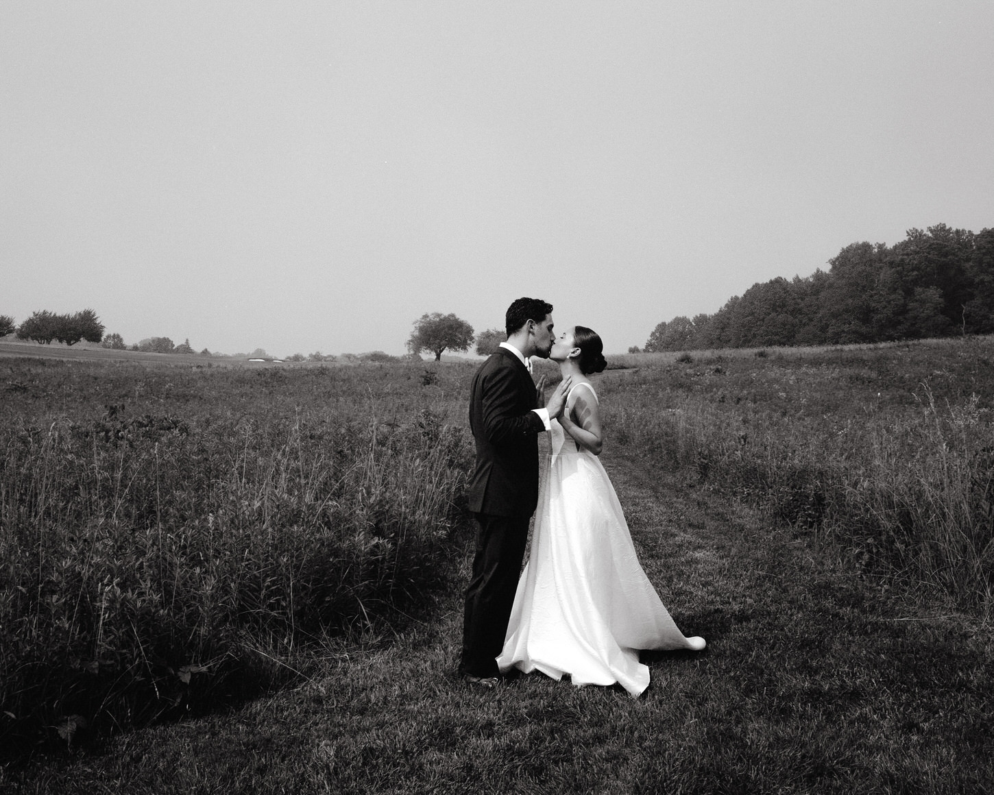 The bride and groom are kissing in the middle of a vast field, captured on film by Jenny Fu Studio.