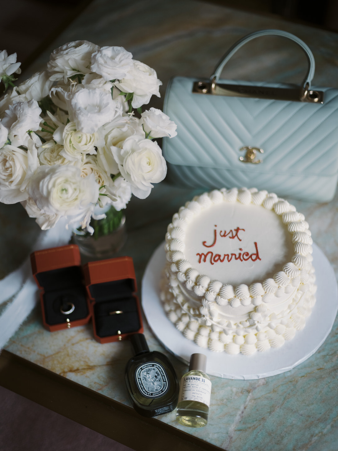 A small, white, wedding cake, bride's bouquet, clutch bag, wedding bands and small bottles of perfumes for an intimate elopement at NYC, captured by Jenny Fu Studio.