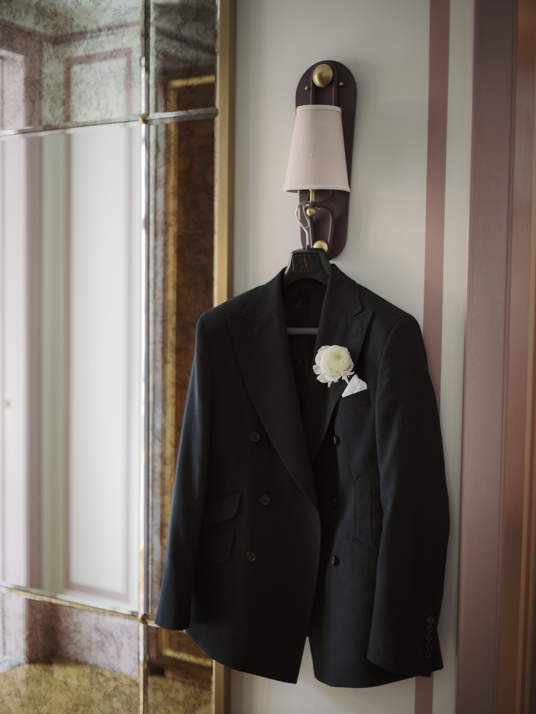 The groom's black suit with white boutonnière is hanging on a hotel room wall for an elopement, captured by Jenny Fu Studio.