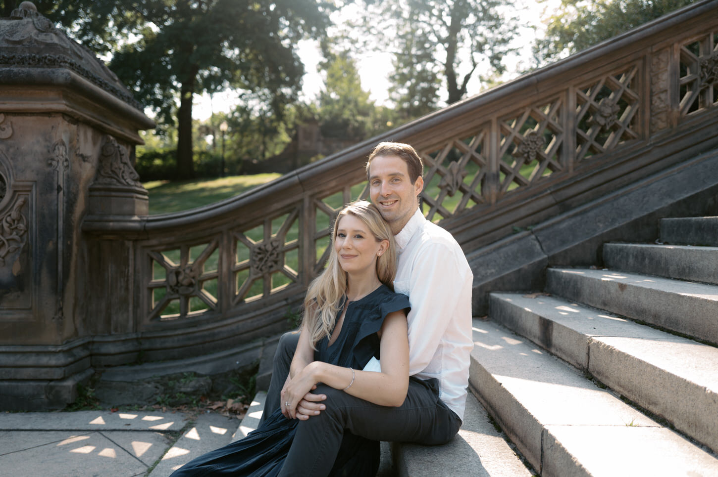 The engaged couple is sitting on a staircase in Central Park, New York, captured by Jenny Fu Studio.