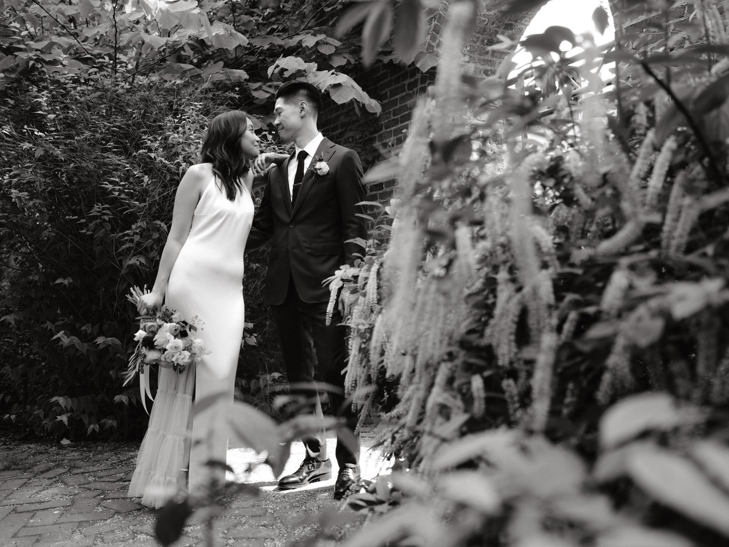 Black and white image of the bride and groom looking at each other's eyes in the middle of a garden, captured by Jenny Fu Studio.