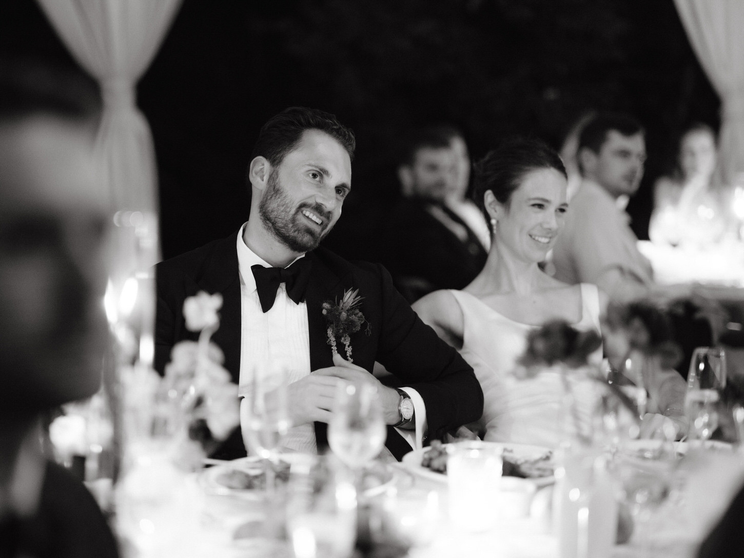 Black and white candid image of the newlyweds as they happily watch the wedding reception program, captured by Jenny Fu Studio.