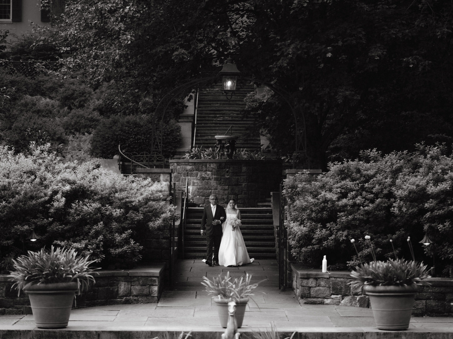 Black and white image of the bride and her father walking towards the aisle, captured in an elegant wedding portrait by Jenny Fu Studio.