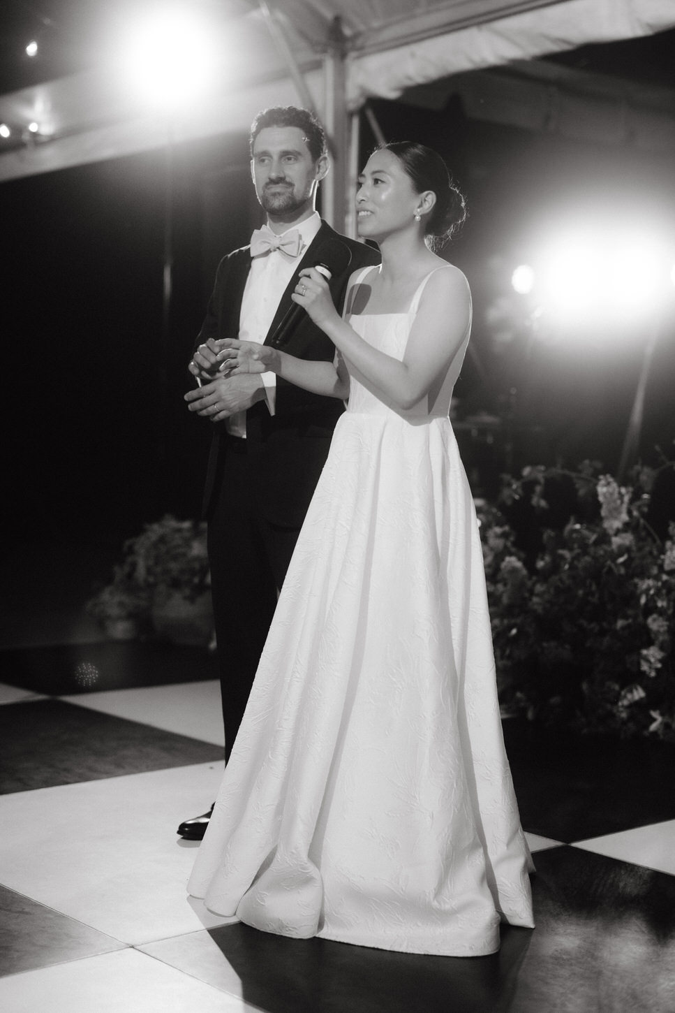 Photojournalistic image of the newlyweds on the stage as the bride gives a speech, captured in an elegant wedding portrait by Jenny Fu Studio.