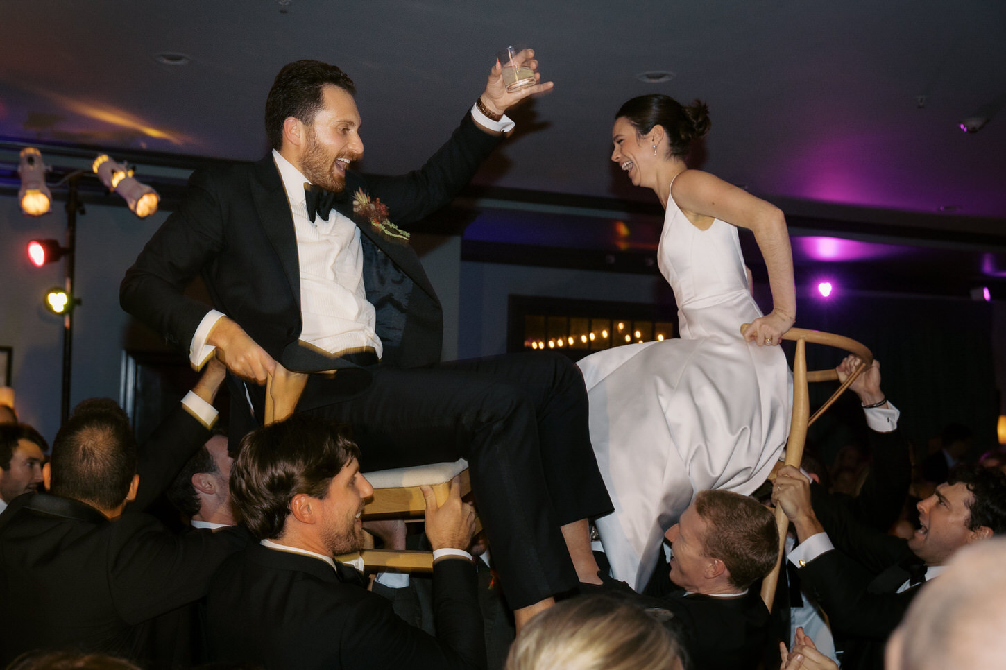 The newlyweds, seated on chairs, are ecstatically raised high above by guests, in the wedding reception, captured by high-fashion wedding photographer Jenny Fu, of Jenny Fu Studio.