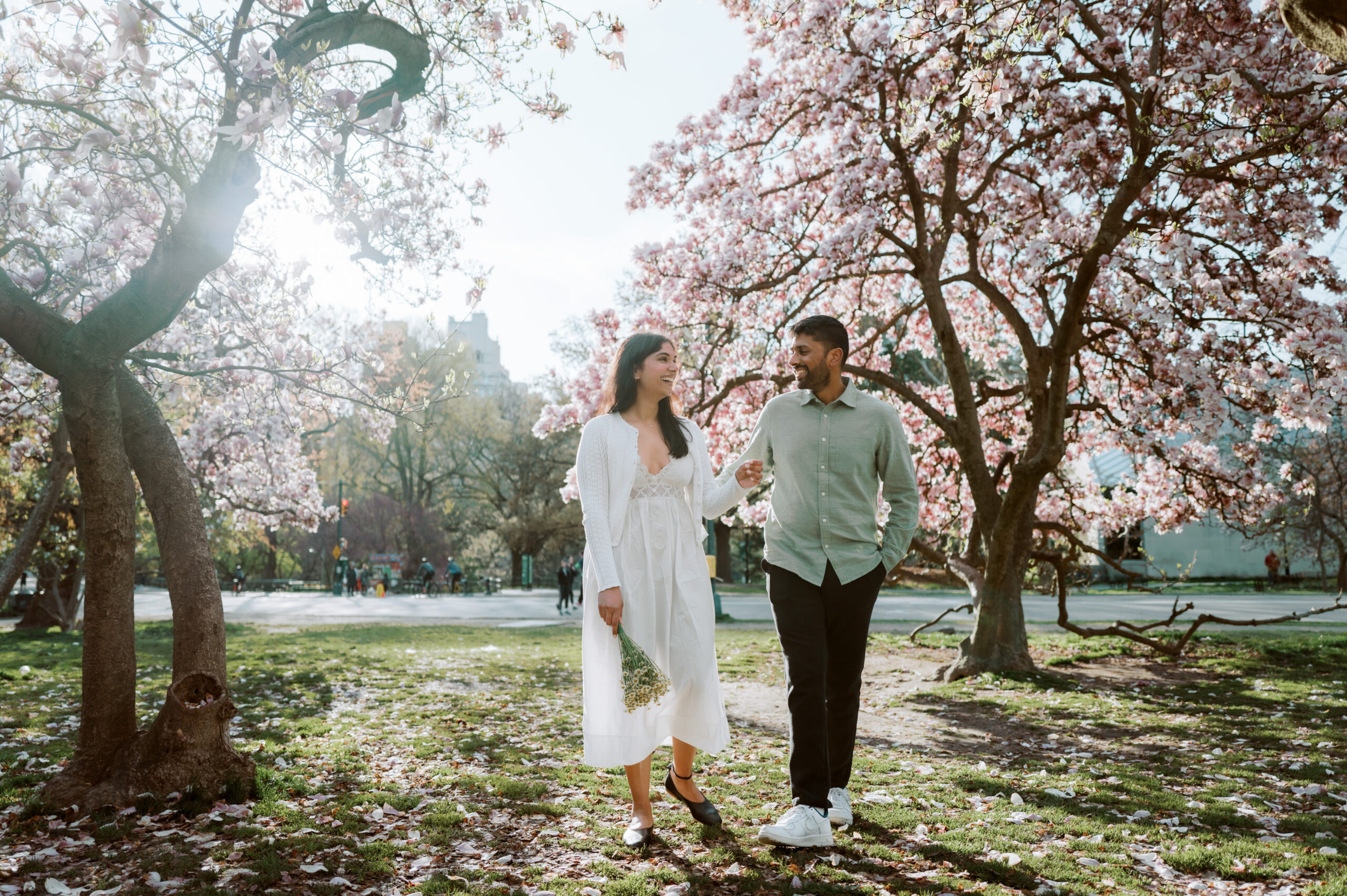 The engaged couple are having a happy and light conversation while strolling in Central Park, NYC during spring, captured by Jenny Fu Studio for an authentic wedding storytelling.