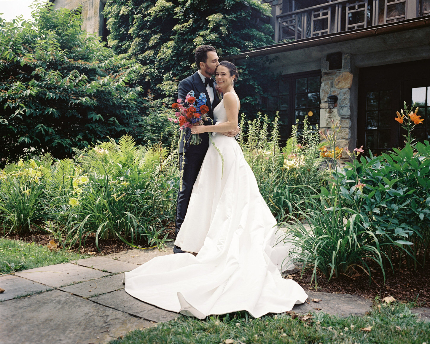 The groom kisses his bride in the forehead in their first look, with a garden in the background, captured by Jenny Fu Studio.