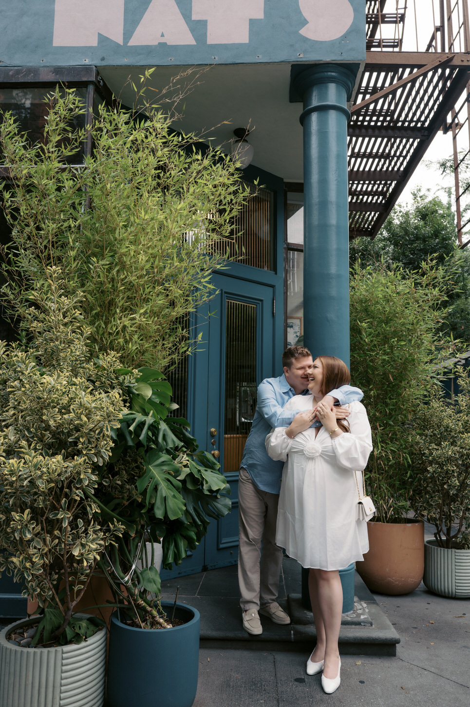 The engaged couple are laughing and having a good time, standing outside Nat's restaurant in NYC, captured by Jenny Fu Studio.