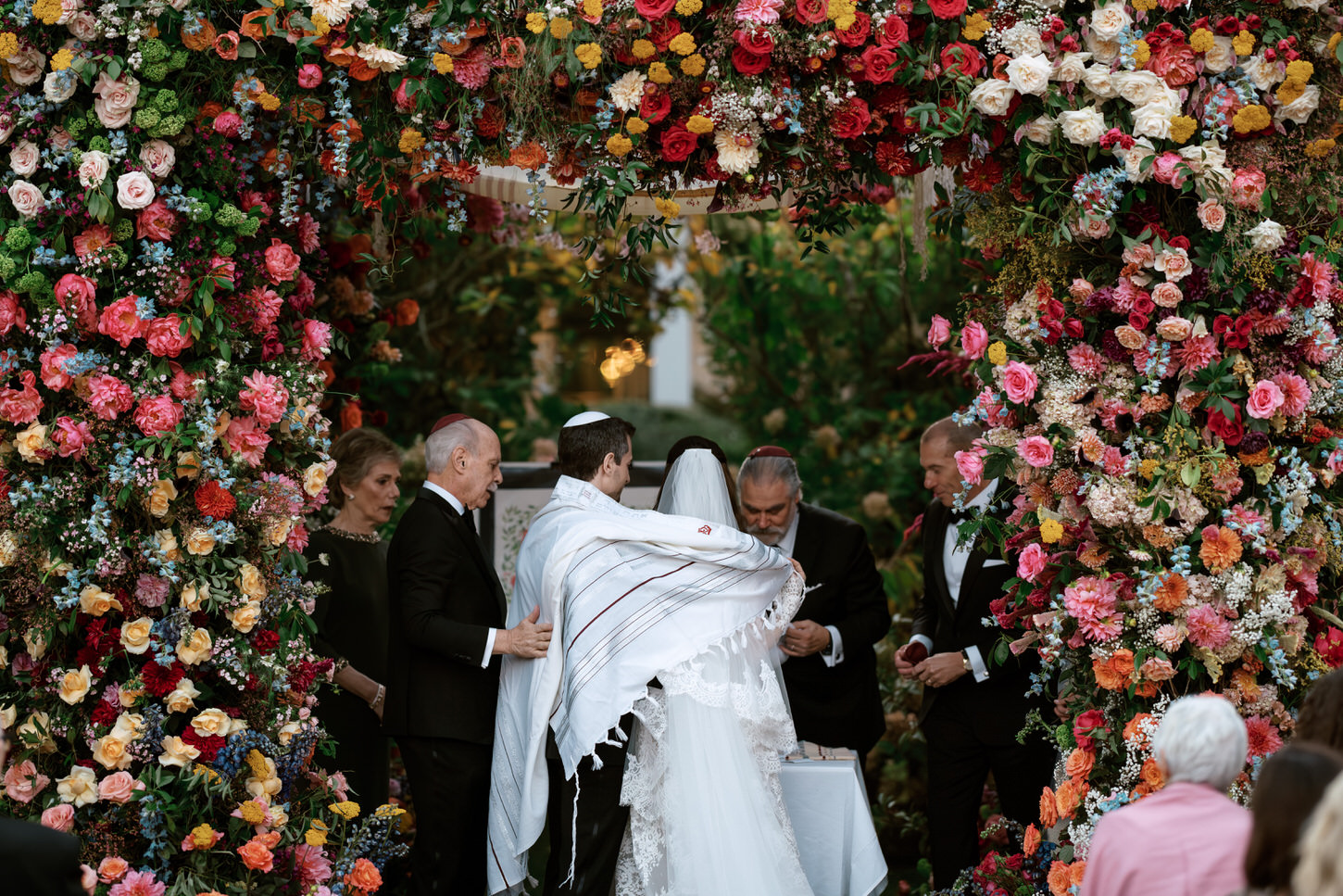 Ethereal wedding moments of a Jewish wedding ceremony in the middle of a magnificent wedding arch overflowing with colorful florals.