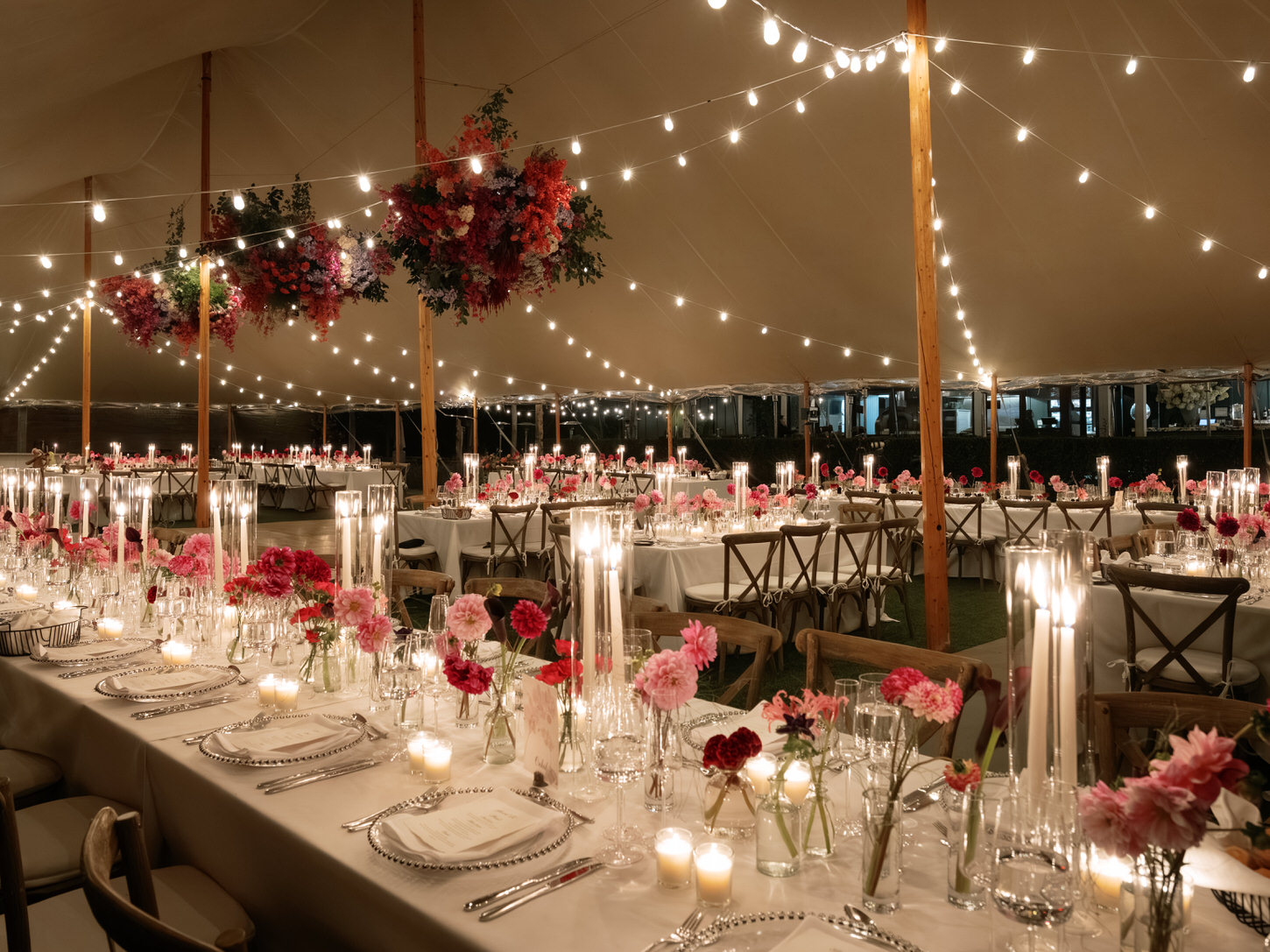 An elegant wedding reception dinner set-up in an outdoor tent full of fairy lights, flowers and candles.