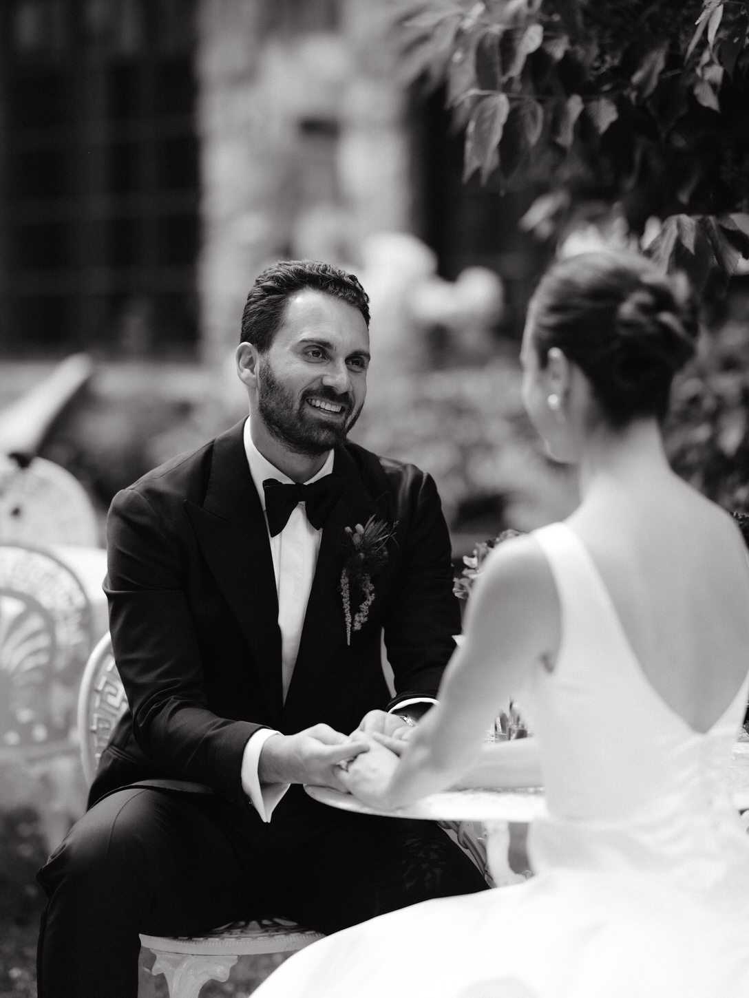 Black and white candid image of the bride and groom, sitting down, holding hands, and simply adoring each other, captured by high-fashion wedding photographer, Jenny fu Studio.
